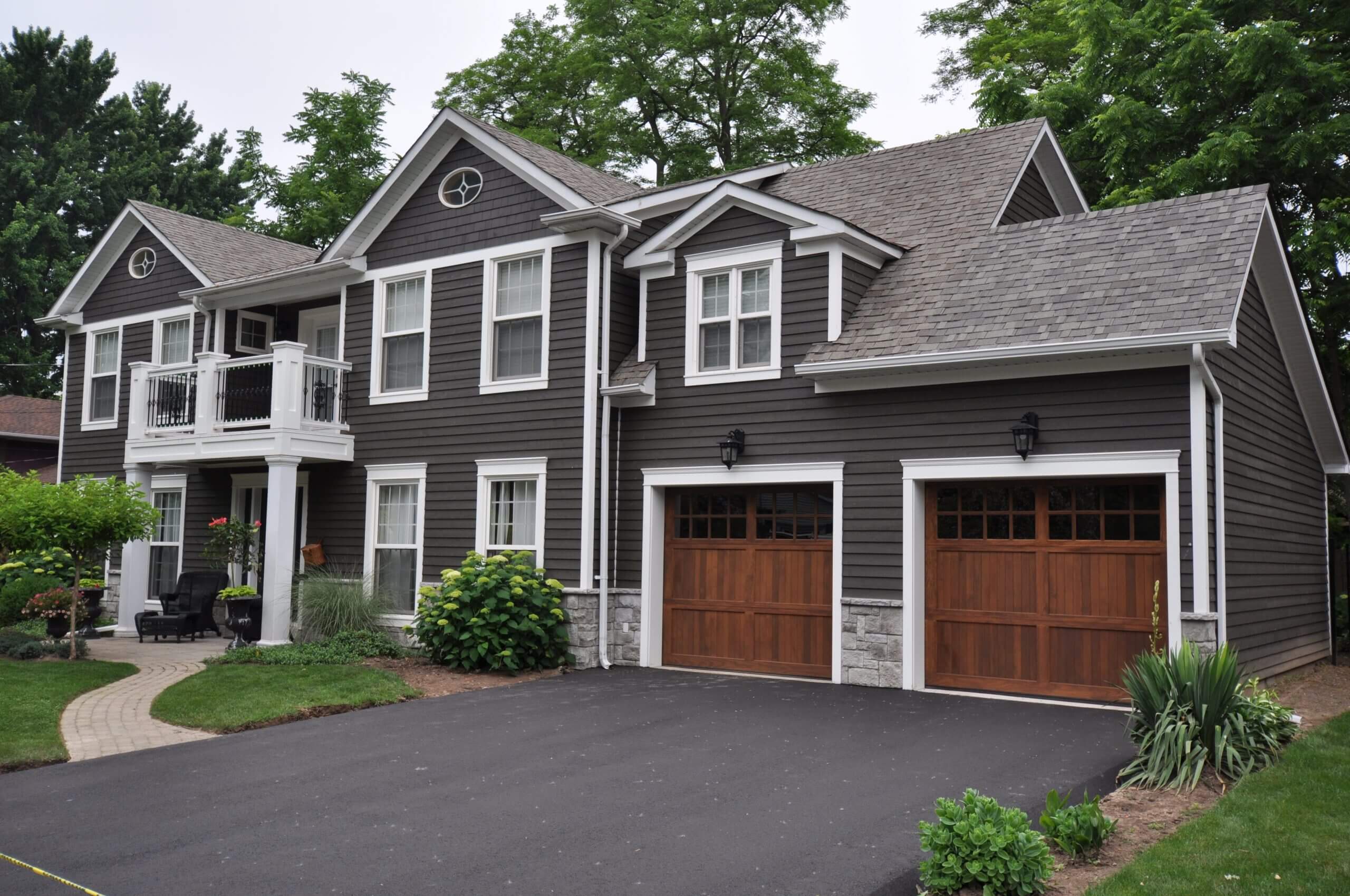 A modern gray house with wooden garage doors and a paved driveway.