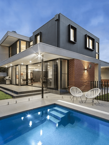 Modern two-story house with pool and outdoor seating area at dusk.