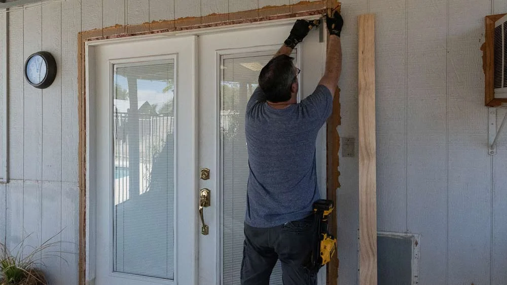 Man installing a wooden frame around a door.