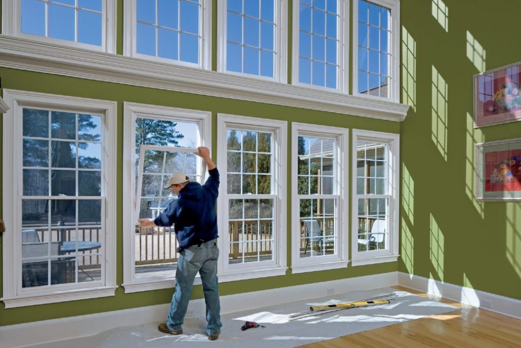 Worker installing or inspecting large windows in a sunlit room.