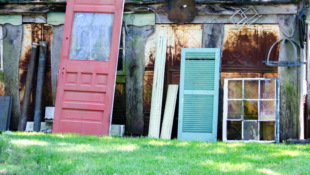 Various old doors and shutters leaning against a wall outdoors.
